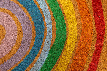 Colorful rainbow arc pattern on natural fiber texture background, circular multi-colored coir doormat surface.