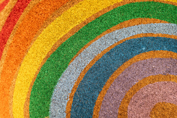 Colorful rainbow arc pattern on natural fiber texture background, circular multi-colored coir doormat surface.