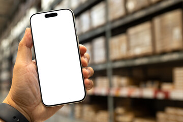 Man hand holding smartphone with blank white screen in blurred warehouse background, AI logistics and inventory management concept. Supply chain logistics, smart warehousing, and online shopping.