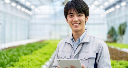 植物工場でタブレットを手に笑顔で立つ若い男性作業員（スマート農業）