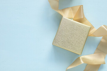 A shimmering golden gift box with a satin ribbon on a soft, light blue wooden background. Concept for celebration, and festive occasions, perfect for holidays, anniversaries, and special moments.