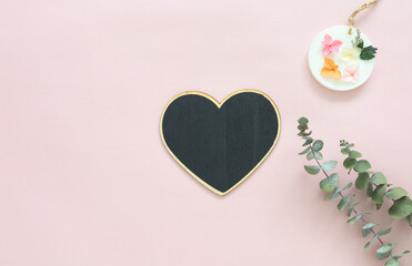 Top view of a black heart shaped chalkboard over a pastel pink background, eucalyptus leaves and a scented wax sachet. Ideal top view for love, greeting cards, mother's day, valentines, concepts.
