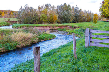 Meandering Geleenbeek River with water flowing in Absbroekbos conservation area, greenish-brown wild grass, winter trees in background, cold day in Munstergeleen, Limburg, Netherlands