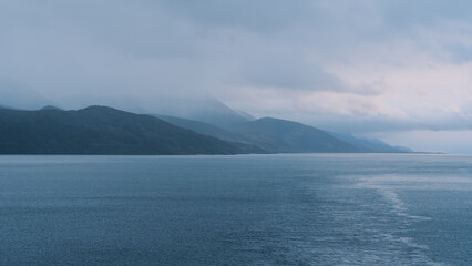 Ushuaia Argentina Tierra del Fuego Magical Mountain Islands Covered In Clouds and Fog at Sunset Dusk. Blue Cool Tone View From Back of Ship Wake