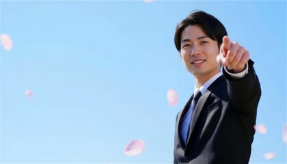 青空と桜を背景に指差すポーズの笑顔の男性ビジネスマン