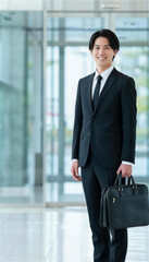 オフィスのロビーでビジネスバッグを持ち笑顔で立つ男性社員