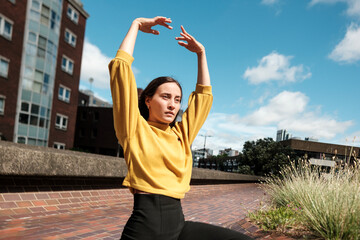 Young woman dancing outdoors in urban setting, raising arms in graceful movement