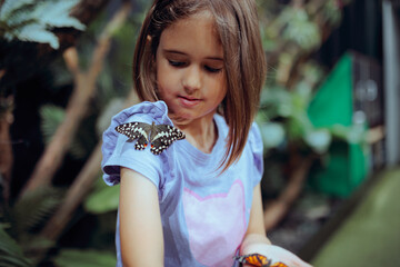 Happy Little Girl Playing with a Lime Butterfly. Cheerful gentle child getting to know exotic insects at a butterfly house