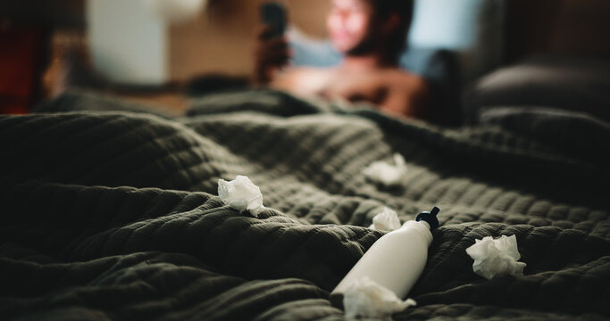 Lotion, tissues and man in bedroom for temptation, self pleasure and masturbation. Night, secret and man with arousal for pornography, addiction and sneaky activity with privacy, home or toilet paper