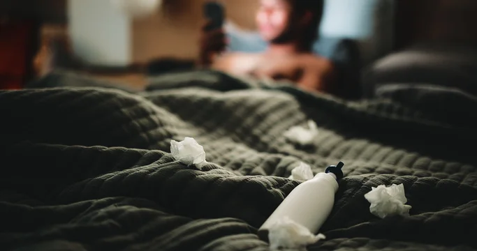 Lotion, tissues and man in bedroom for temptation, self pleasure and masturbation. Night, secret and man with arousal for pornography, addiction and sneaky activity with privacy, home or toilet paper