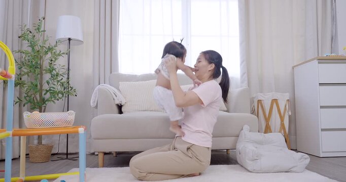 Asian mother lifts toddler girl in arms with smile, joyful embrace after meal, warm daylight in living room, love and care, emotional family bonding, early childhood happiness, cozy home lifestyle