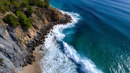 Aerial view of a coastal cliff with turquoise ocean waves crashing against rocks.