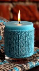 Warm lit blue candle in a knitted cozy holder on a textured blanket