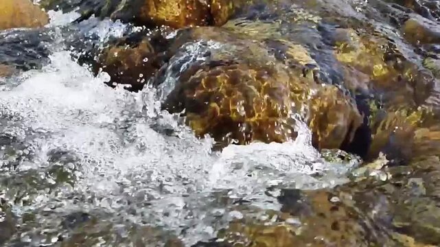 Slow motion close-up shot of fresh water flowing over rocks in a small stream **in Morocco**. The natural brook scene captures the movement of the clear current.