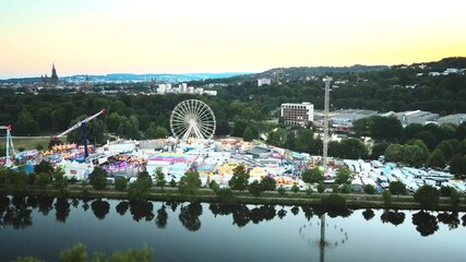 Captivating drone orbit circles Ulm Volksfest's massive ferris wheel and vibrant fairground along Danube River, framing Ulm Minster's twin spires at golden hour. Ultimate festival spectacle.