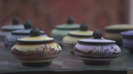 Close-up shot of traditional handmade ceramic jars displayed in a shop. The pottery features hand-painted Moroccan landscapes and colorful glazes in the souk.