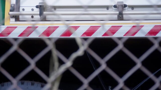 Side of a Rural Fire Truck behind a secured chain link fence. Sliding left to right clip, focused on the side hazard stripe.