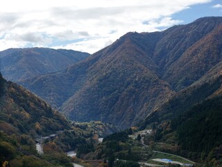 The mountains are covered in a lush green forest, with trees of various sizes and shapes. The sky above is cloudy, creating a moody atmosphere. The scene is peaceful and serene
