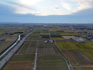 A large field of crops is shown from above. The sky is cloudy and the sun is setting