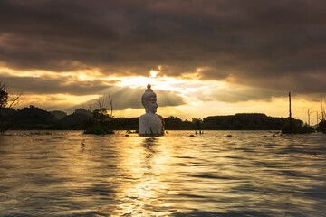 Golden sunset over seated buddha statue in water (Phra Chom Nam) in Khao Rakham Reservoir at Trat Province of Thailand