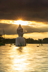 Golden sunset over seated buddha statue in water (Phra Chom Nam) in Khao Rakham Reservoir at Trat Province of Thailand