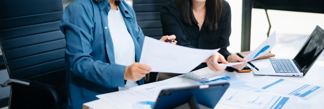 Asian senior and middle aged businesswomen reviewing documents and reports in office. Professional teamwork, mentorship, business collaboration - Powered by Adobe