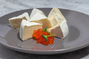 Plate of soft cheese wedges with red caviar on a gray background