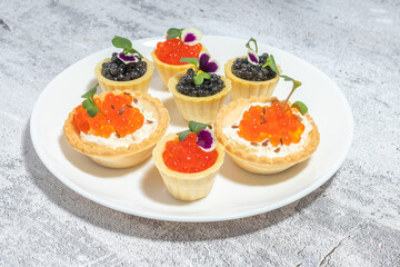 Assorted gourmet caviar tartlets beautifully arranged on a white plate, garnished with fresh herbs and edible flowers, set on a textured gray surface.