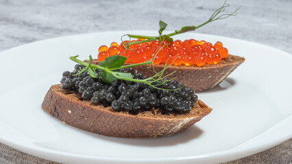 Two slices of bread with black and red caviar, garnished with greens, served on a white plate.