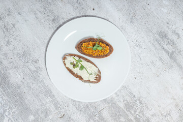 Top view of two gourmet open-faced sandwiches on a white plate with rustic background, showcasing culinary artistry and minimalist presentation.