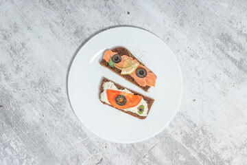 Top view of gourmet open-faced sandwiches with cream cheese, smoked salmon, and vegetables on a white plate against a textured background