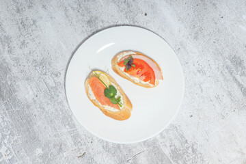 Two gourmet bruschetta with salmon and tomato on a white plate over a rustic background.
