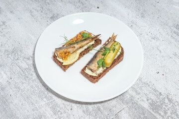 Open-faced sandwiches with sardines, mustard seeds, and lemon on rye bread served on a white plate