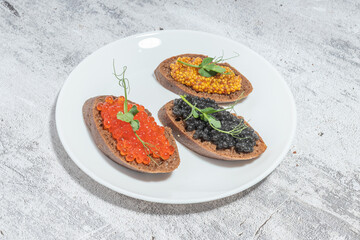 Assorted caviar toasts on a white plate with a rustic background
