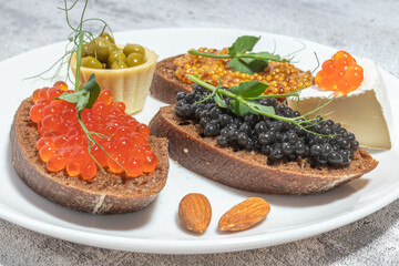 An elegant arrangement of gourmet snacks featuring caviar, cheese, and almonds on a white plate.