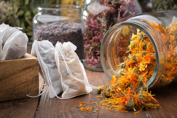 Glass jar of dry calendula flowers for making herbal tea. Filter tea bags filled with medicinal herbs. Jars of various healthy herbs in the background. Alternative medicine.