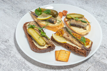 Plate with assorted open-faced fish sandwiches garnished with pickles and herbs on a light background