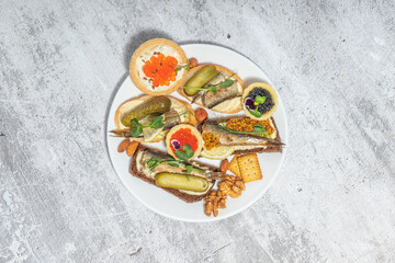 Assorted gourmet appetizers on a white plate including fish, caviar, and pickles, presented on a textured table surface.