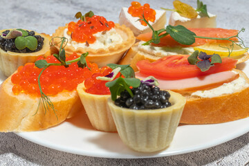 An assortment of gourmet appetizers with caviar, salmon, and fresh vegetables on a white plate.