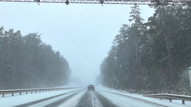 Cars navigate a snowy highway in difficult conditions. Snow covers the road and visibility is low. The weather creates challenges for all drivers present.