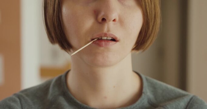 Close-up of a woman holding a toothpick in her mouth, relaxed and casual expression &mdash; concept of daily habits, oral care, or casual attitude.