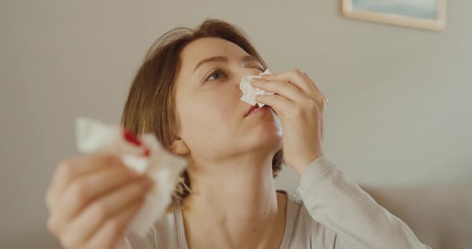 A woman sitting at home treating a sudden nosebleed with tissues &mdash; concept of minor health issue, first aid, and everyday medical care.