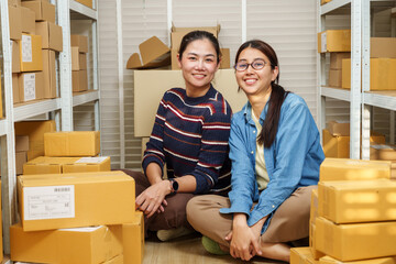 Asian adult women small business owners sitting together after online shop order packing inside home warehouse representing successful ecommerce teamwork calm moment and online seller daily work