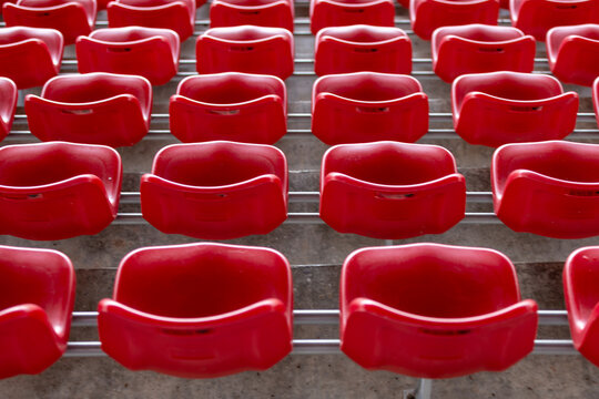 Empty rows of red plastic stadium seats create a repetitive pattern in a vacant sports arena before an event - Powered by Adobe
