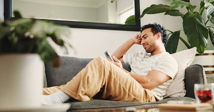 Home, relax and man on sofa, smartphone and texting with social media, internet or connection. Apartment, mobile user or Asian person on couch, cellphone or network with digital app for communication - Powered by Adobe