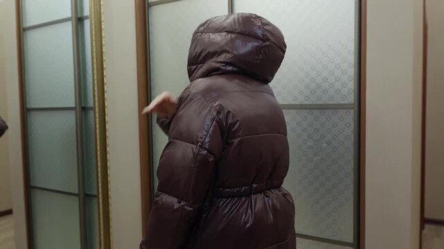 Young woman in brown padded jacket brushing dust off coat with hand indoors, calm practical mood symbolizing clothing maintenance and everyday life.
