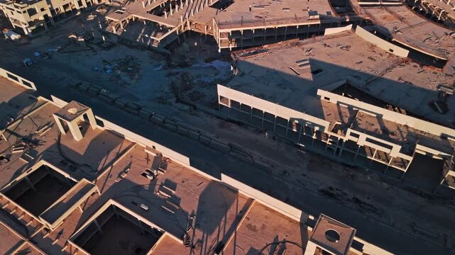 Cinematic 4K drone aerial of unfinished concrete complex with courtyards, rooftop openings, debris and long golden-hour shadows&mdash;ideal for development and real estate visuals.