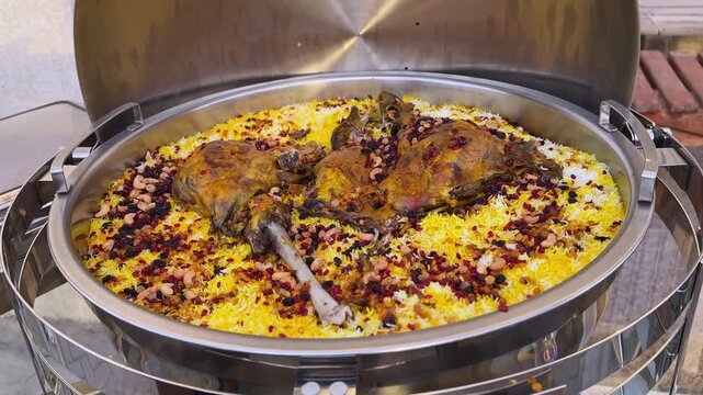 Close-up of Middle Eastern lamb mandi kabsa: saffron basmati rice topped with roasted meat, nuts and dried berries in a stainless buffet chafing dish for catering and events.