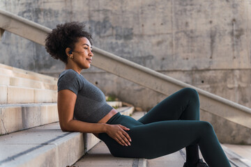Young athletic woman unwinds on the stairs with wireless earbuds, enjoying music after her workout