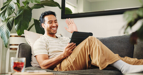 Man, tablet and video call on sofa, wave and happy with conversation in living room at home. Person, tech and smile with application, virtual chat and hello on web, couch or scroll at apartment © peopleimages.com